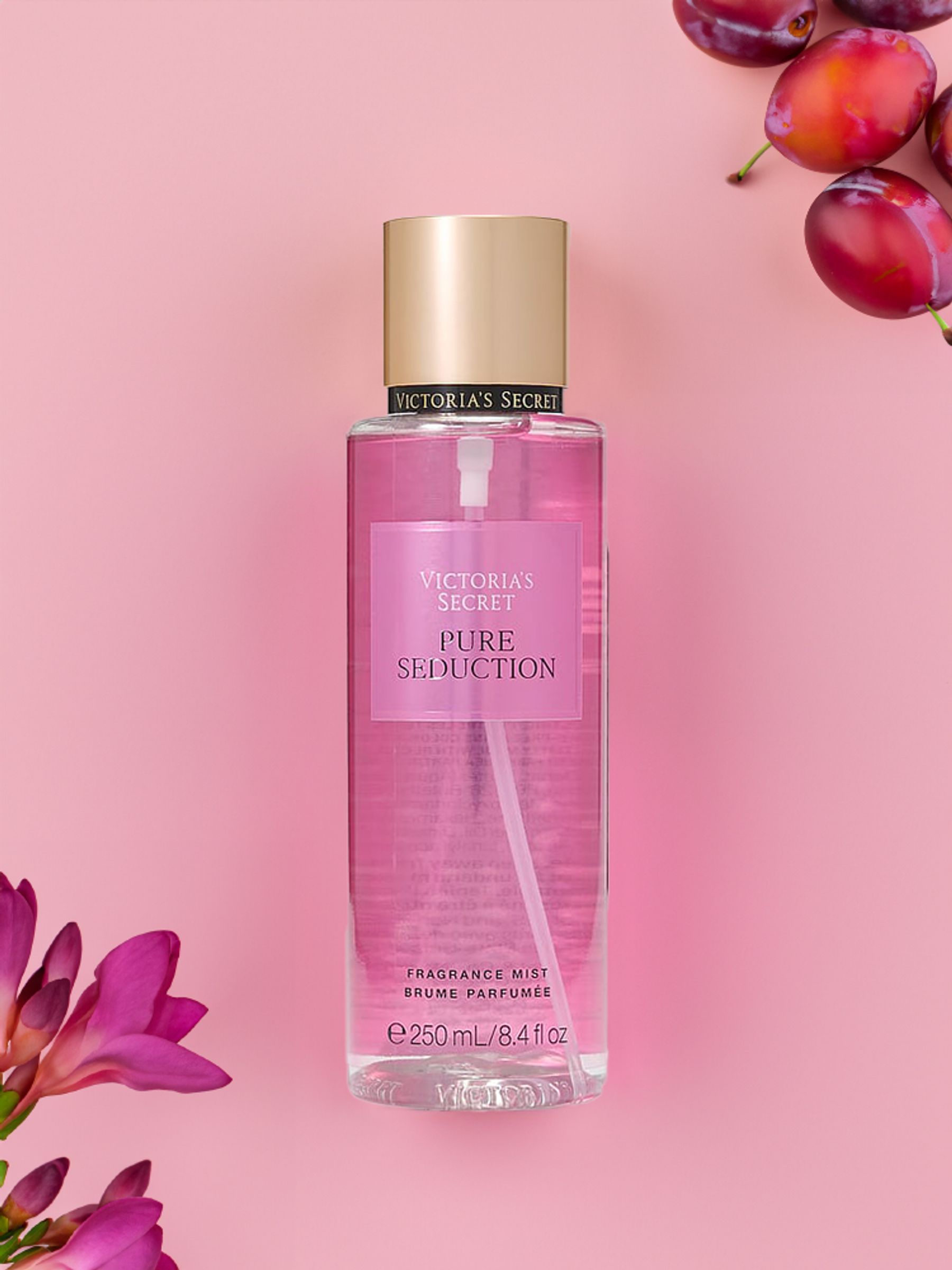 Body mist Victoria's Secret Pure Seduction de 250 ml en flat lay con ciruelas y flores rosadas.