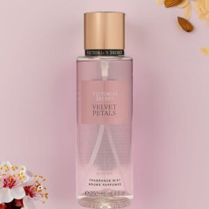 Body mist Victoria's Secret Velvet Petals junto a almendras laminadas y flores de cerezo sobre fondo rosa.