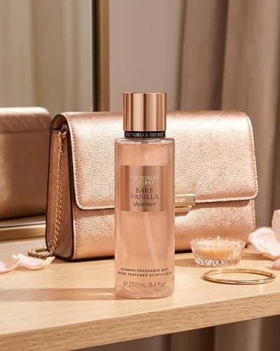 Body mist Victoria's Secret Bare Vanilla de 250 ml sobre mesa de madera junto a una cartera rosa y una vela.