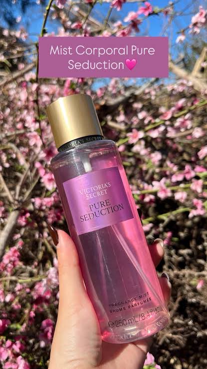 Body mist Victoria's Secret Pure Seduction de 250 ml sostenido en mano con flores rosadas de fondo.