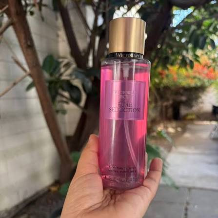 Mano sosteniendo el body mist Victoria's Secret Pure Seduction de 250 ml al aire libre.