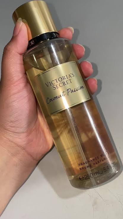 Mano sosteniendo el body mist Victoria's Secret Coconut Passion de 250 ml sobre fondo gris.